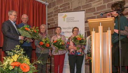 Mehrere Vereinsmitglieder des Diakonieverein Werratal e.V. stehen auf der Bühne mit Blumensträußen in den Händen beim Zusammenschluss von Diakonie Werratal und Immanuel Diakonie Südthüringen im Kressehof im Meininger Ortsteil Walldorf